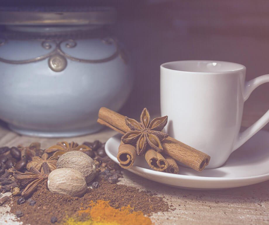 Teetasse mit Gewürzen als Deko, im Hintergrund alte Teekanne aus Ton